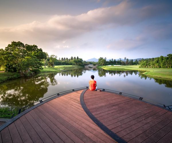 Person meditating peacefully outdoors near a calm lake at sunrise.
